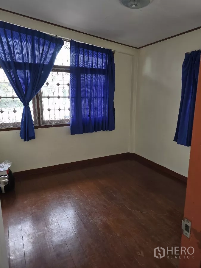 Home Office for rent in Wang Thonglang, Bangkok - Compact bedroom with polished wood flooring, barred windows and blue curtains.