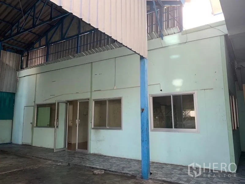 Warehouse for rent or sale in Bang Na, Bangkok - Ground-floor office entrance beneath mezzanine inside a light-green warehouse building.