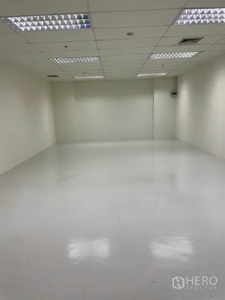 Office Space for rent in Khlong Toei, Bangkok - Spacious empty office room with white flooring, cream walls and fluorescent drop-ceiling lights.