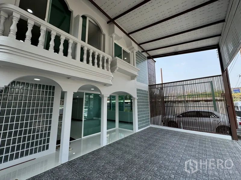 Townhouse for sale in Bueng Kum, Bangkok - Angled view of driveway with metal privacy gate and arched windows of the townhouse.