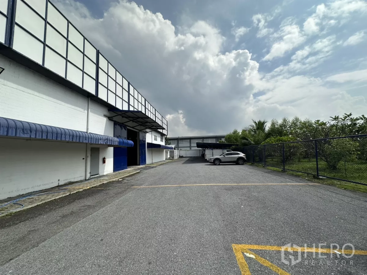 คลังสินค้า ให้เช่าในPhra Khanong, Bangkok - ถนนภายในและที่จอดรถกว้างข้างโกดัง พร้อมรั้วและต้นไม้ แสดงทางเข้าขนถ่ายสินค้า