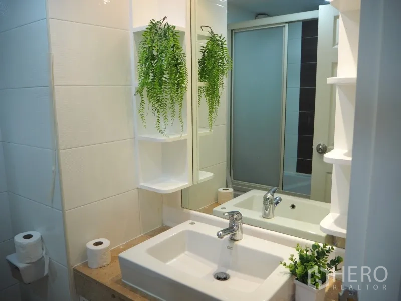 Condominium for rent or sale in Watthana, Bangkok - Contemporary bathroom vanity with large mirror, white basin, and hanging greenery.