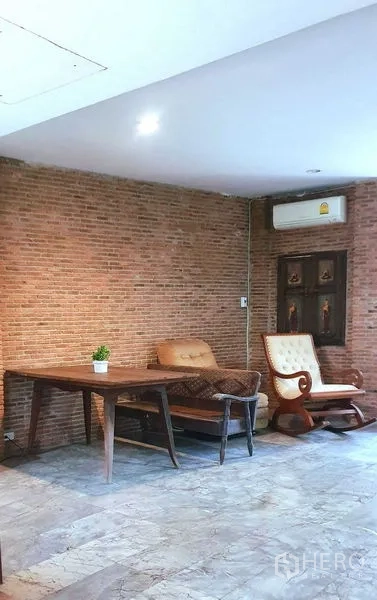 Townhouse for rent or sale in Suan Luang, Bangkok - Lounge with exposed brick feature wall, wooden furniture and air conditioning.