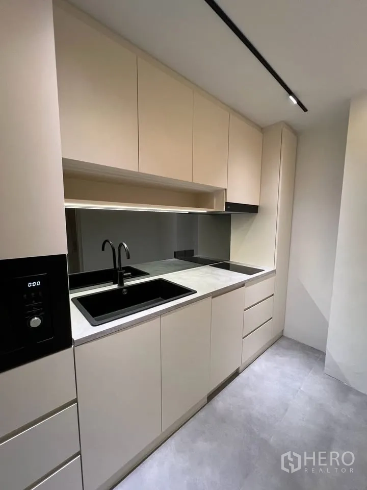 Townhouse for rent in Prawet, Bangkok - Galley kitchen with beige cabinets, black sink and induction hob.