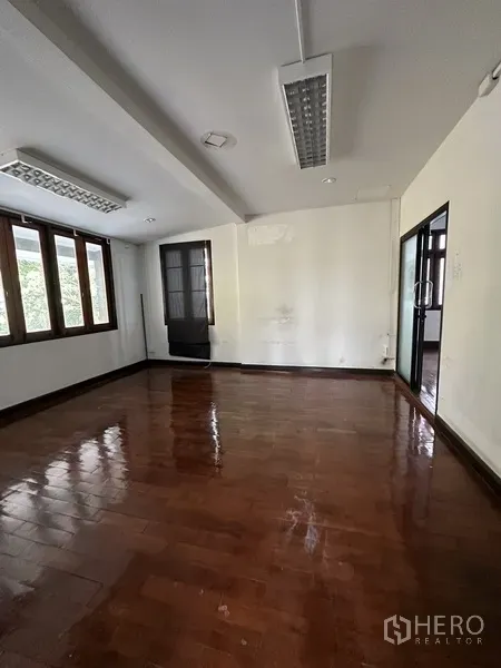 Detached House for rent in Phaya Thai, Bangkok - Empty room with polished wooden floor, fluorescent lighting and windows on two sides.