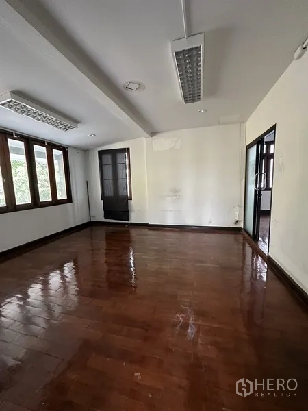 Detached House for rent in Phaya Thai, Bangkok - Empty room with polished wooden floor, fluorescent lighting and windows on two sides.