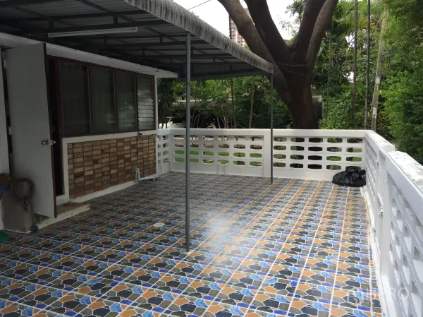Townhouse for rent in Yan Nawa, Bangkok - Large tiled terrace with awning and white railing facing a green garden.