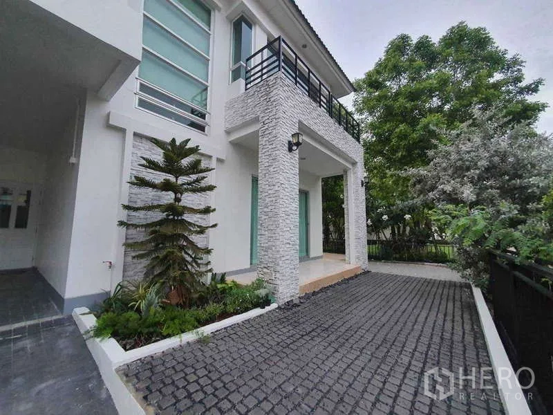 Detached House for rent in Saphan Sung, Bangkok - Facade detail with stone‑clad columns, balcony and cobblestone driveway.