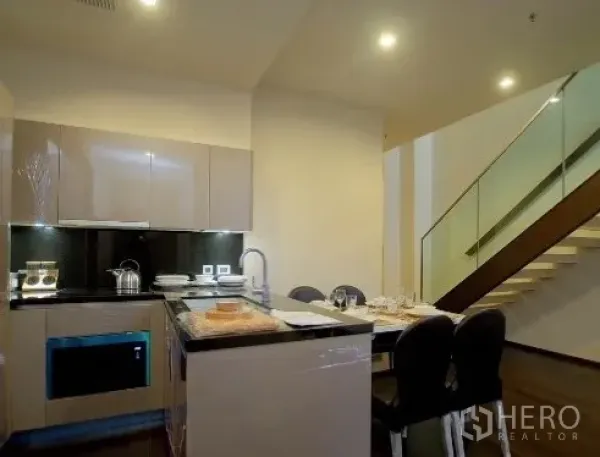 公寓 出租在Watthana, Bangkok - 开放式现代厨房，石材台面、亮面橱柜与餐桌，旁接楼梯。