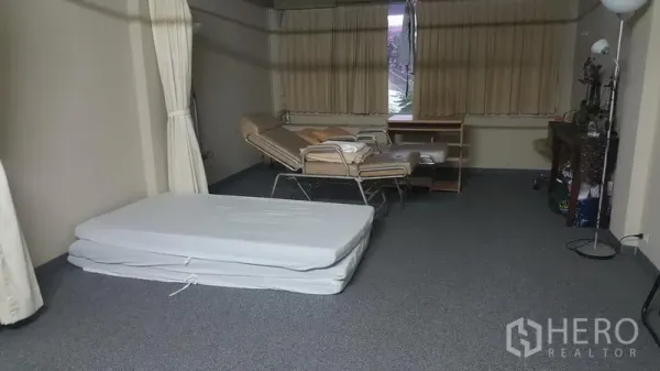 Shophouse for sale in Khlong Toei, Bangkok - Spacious multipurpose room with foldable mattress, reclining chair, desk, carpet flooring and curtained windows.