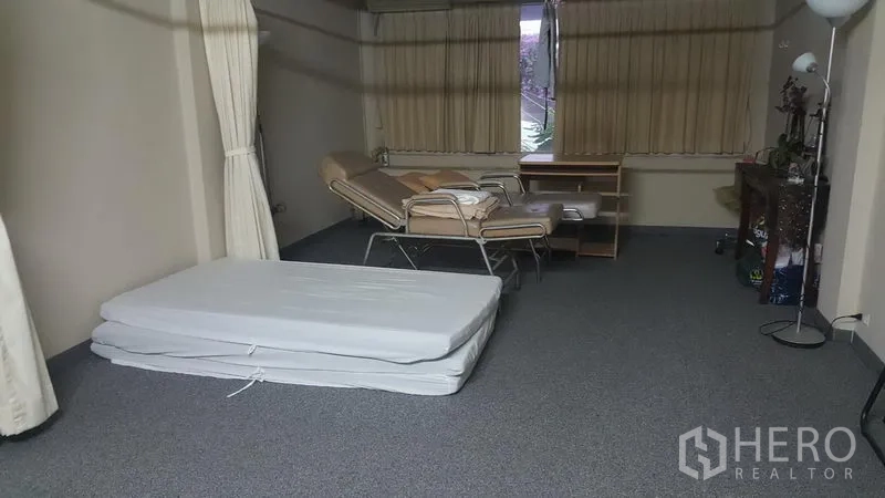 Shophouse for sale in Khlong Toei, Bangkok - Spacious multipurpose room with foldable mattress, reclining chair, desk, carpet flooring and curtained windows.