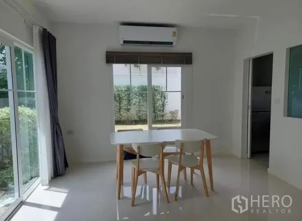 Detached House for rent in Bang Bo, Samut Prakan - Minimal dining area with a white table and four chairs beside large sliding doors.