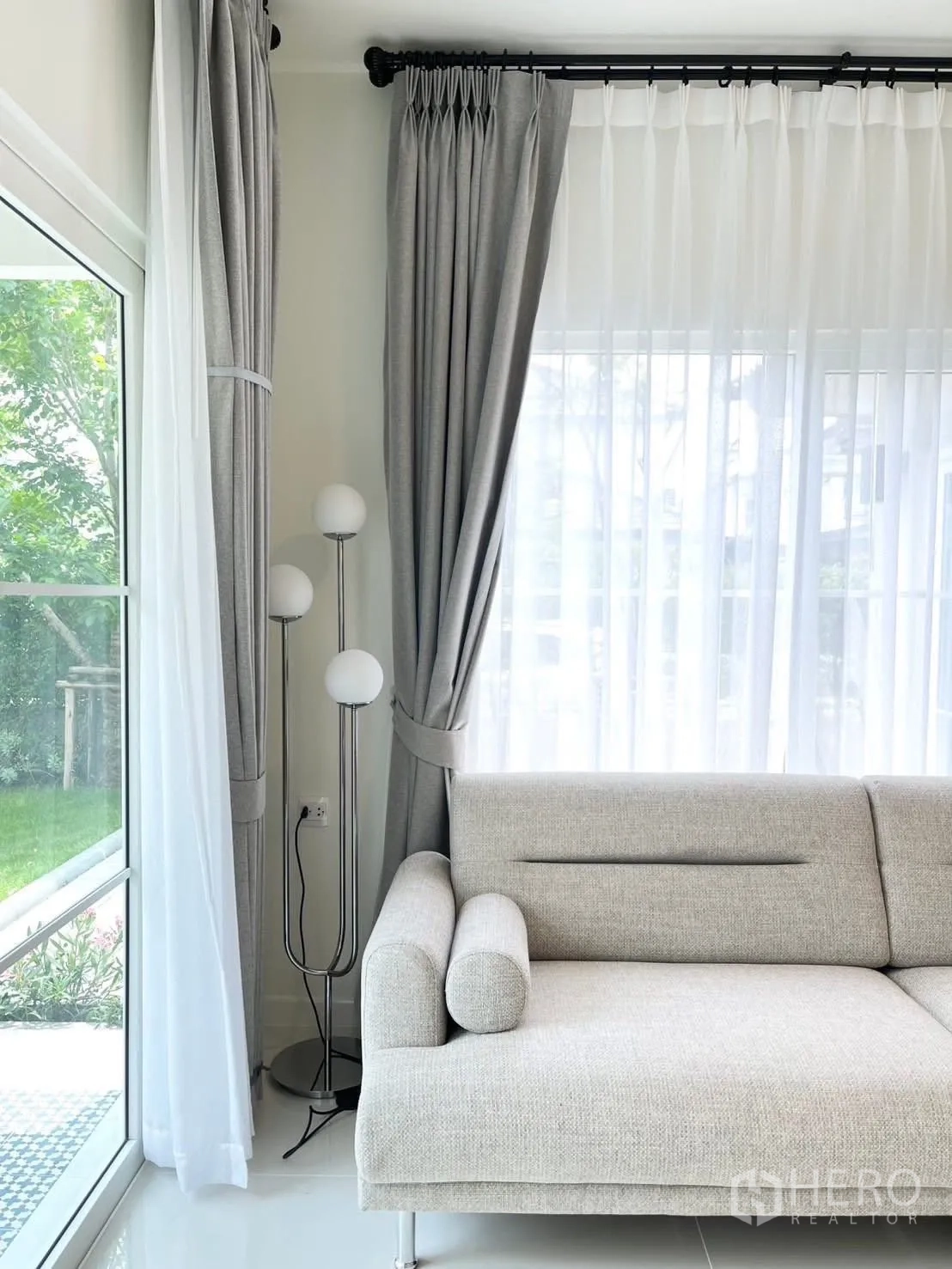 Detached House for rent in Bang Phli, Samut Prakan - Living room sofa beside tall windows, a floor lamp, and garden view.