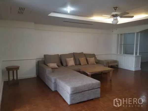 Condominium for rent in Watthana, Bangkok - Spacious living room with large sectional sofa, ceiling fan, and parquet flooring.