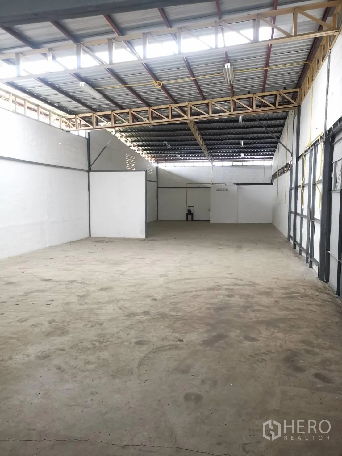 Warehouse for rent in Suan Luang, Bangkok - Open warehouse interior showing high metal roof with skylight strips, white walls and concrete floor.