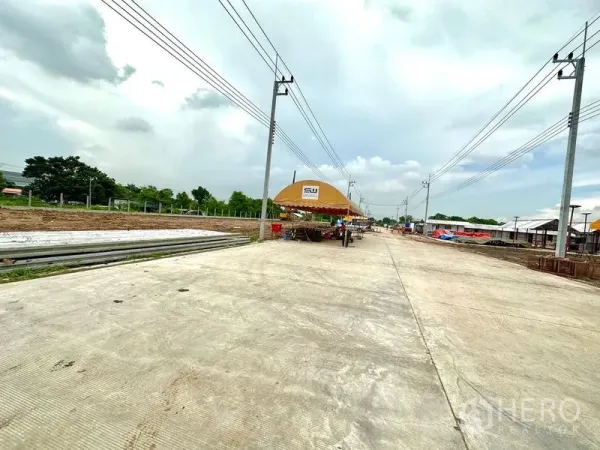 Land for sale in Lam Luk Ka, Pathum Thani - Concrete access road through an industrial development with utility poles, tents and stacked construction materials.
