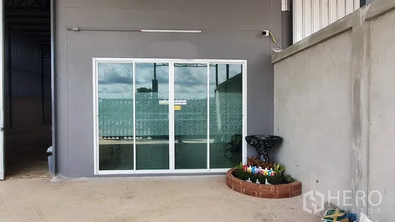 คลังสินค้า ให้เช่าในLam Luk Ka, Pathum Thani - ประตูกระจกบานเลื่อนทางเข้าออฟฟิศ ติดกับลานคอนกรีตและแปลงต้นไม้