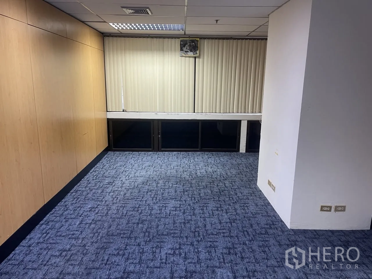 Office Space for rent in Khlong Toei, Bangkok - Smaller office area with blue carpet, vertical blinds, and light wood feature wall.