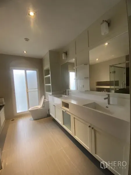 Apartment for rent in Pathum Wan, Bangkok - Modern bathroom with double vanity, oversized mirror and frosted glass door to balcony.