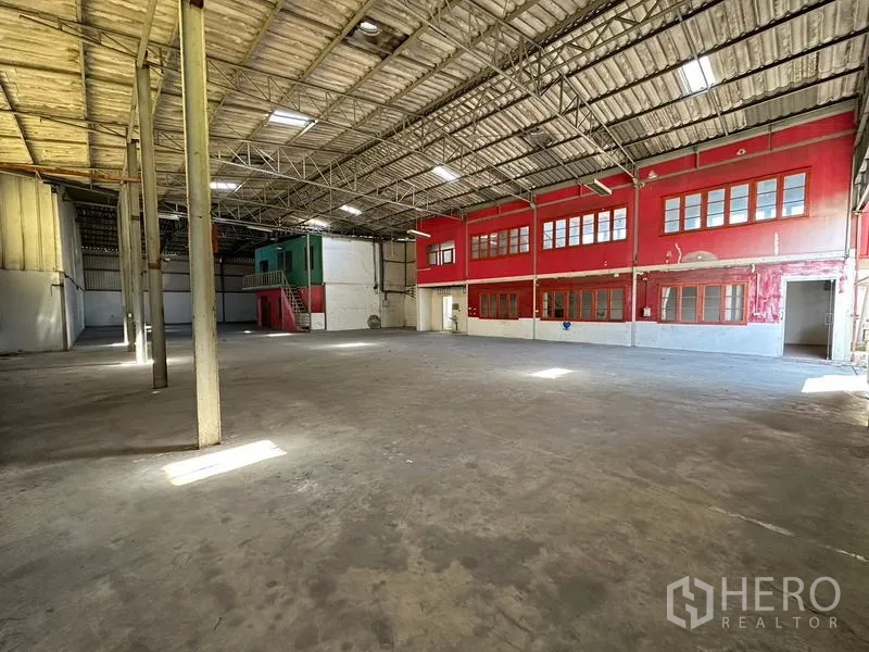 Warehouse for rent in Suan Luang, Bangkok - Open industrial space with steel trusses, skylights and red office rooms along one side.