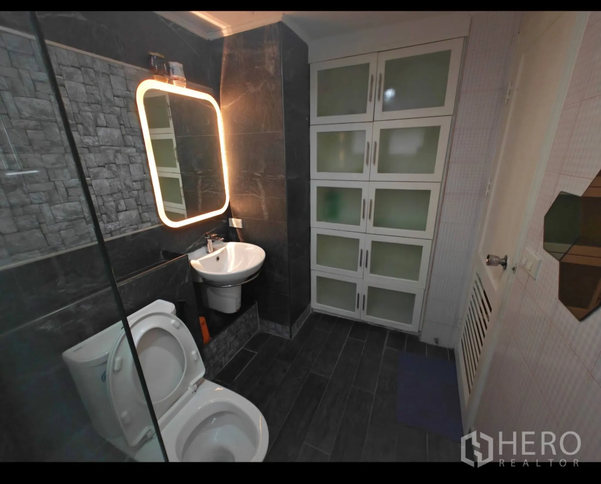 Condominium for rent in Sathon, Bangkok - Modern bathroom with stone-effect tiles, illuminated mirror, glass shower screen, and storage cabinets.