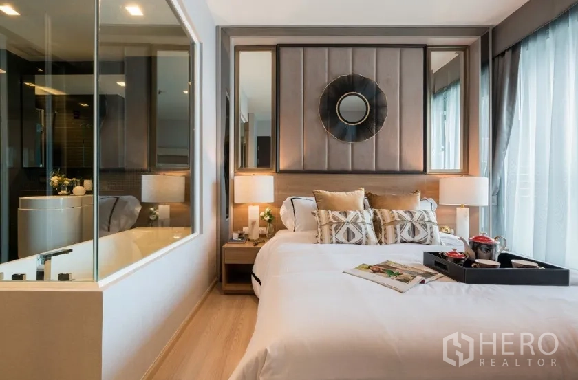 Condominium for rent in Sathon, Bangkok - Cozy bedroom with upholstered headboard, large windows and glass-partitioned bathroom with bathtub.