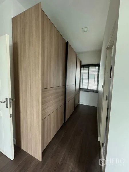 Detached House for rent in Samut Prakan - Hallway with floor-to-ceiling wooden wardrobes and dark wood flooring.