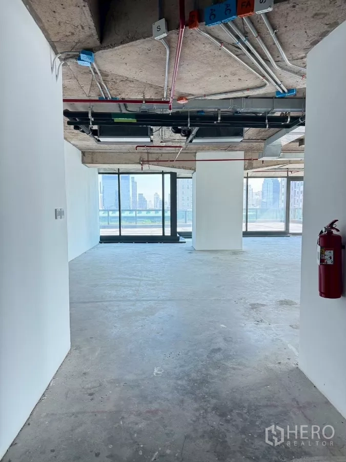 办公空间 出租在Din Daeng, Bangkok - 未装修办公楼层，混凝土地面，消防管线可见，宽幅玻璃面向阳台。