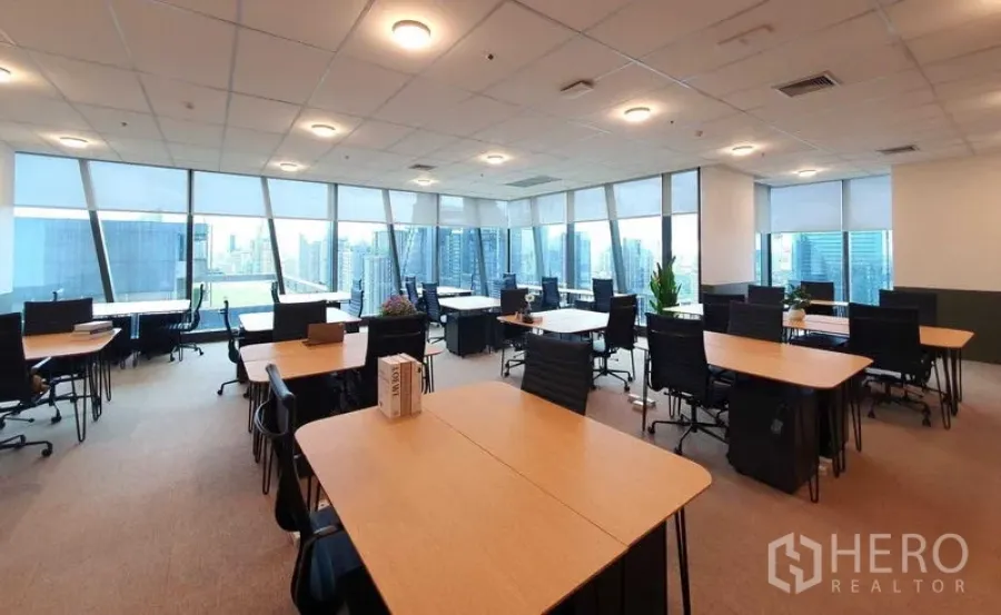 Office Space for rent - Open-plan office on a high floor at G Tower with large windows, city skyline views, wood desks, black chairs, and carpet flooring.