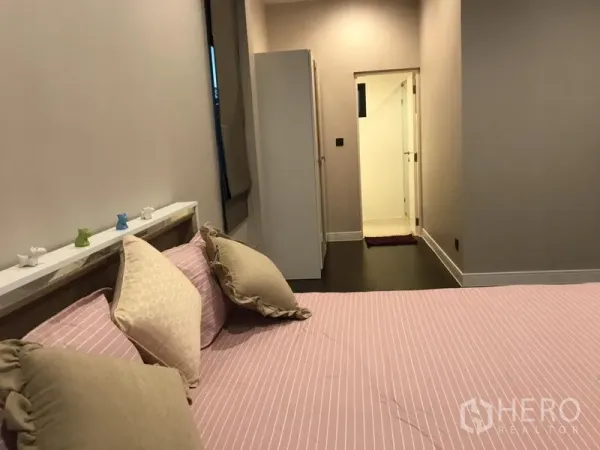 Detached House for rent in Bang Kapi, Bangkok - Cozy bedroom with pink bedding leading to an ensuite bathroom via a short corridor.