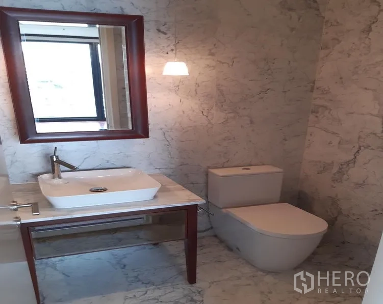 Condominium for rent in Watthana, Bangkok - Marble-clad bathroom with vessel sink, mirror, pendant light and modern toilet.