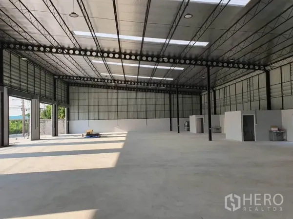 Warehouse for rent in Nonthaburi - Spacious warehouse interior showing high 7.8–6 m ceiling, steel trusses, skylights, and smooth concrete floor.