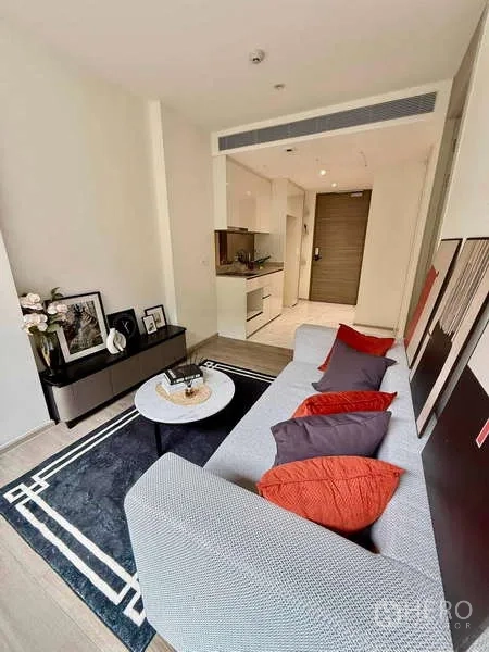 Condominium for rent - Cozy living area facing the entry and kitchenette, with a gray sofa and red accent pillows.