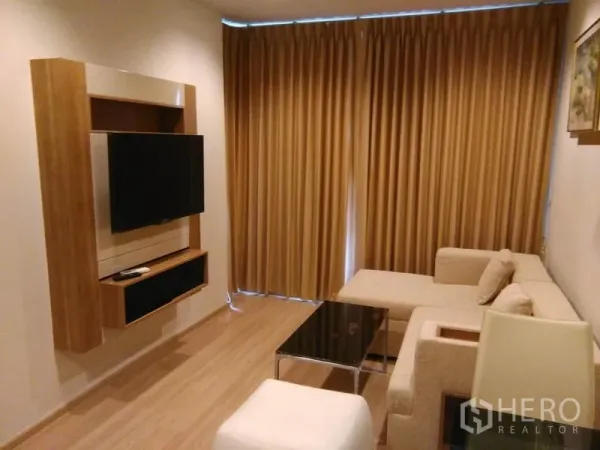 Condominium for rent in Sathon, Bangkok - Cozy living room with L-shaped sofa, mounted TV and blackout curtains.