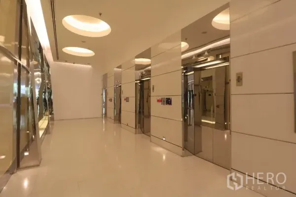 办公空间 出租在Bang Rak, Bangkok - 现代电梯大堂，配多部不锈钢电梯与圆形嵌灯。