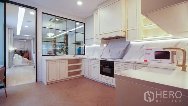 บ้าน ให้เช่าในSaphan Sung, Bangkok - ครัวรูปตัวแอลสไตล์โมเดิร์น ผนังลายหินอ่อน ตู้สีครีม และฉากกั้นกระจกติดกับโซนทานอาหาร