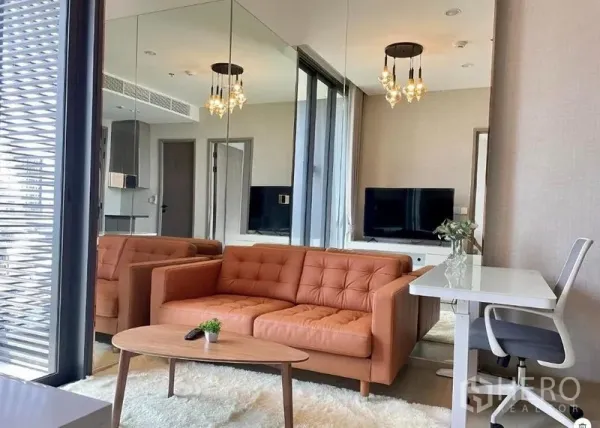 Condominium for rent in Ratchathewi, Bangkok - Living room with orange sofa, work desk, mirrored wall and louvered balcony screen.