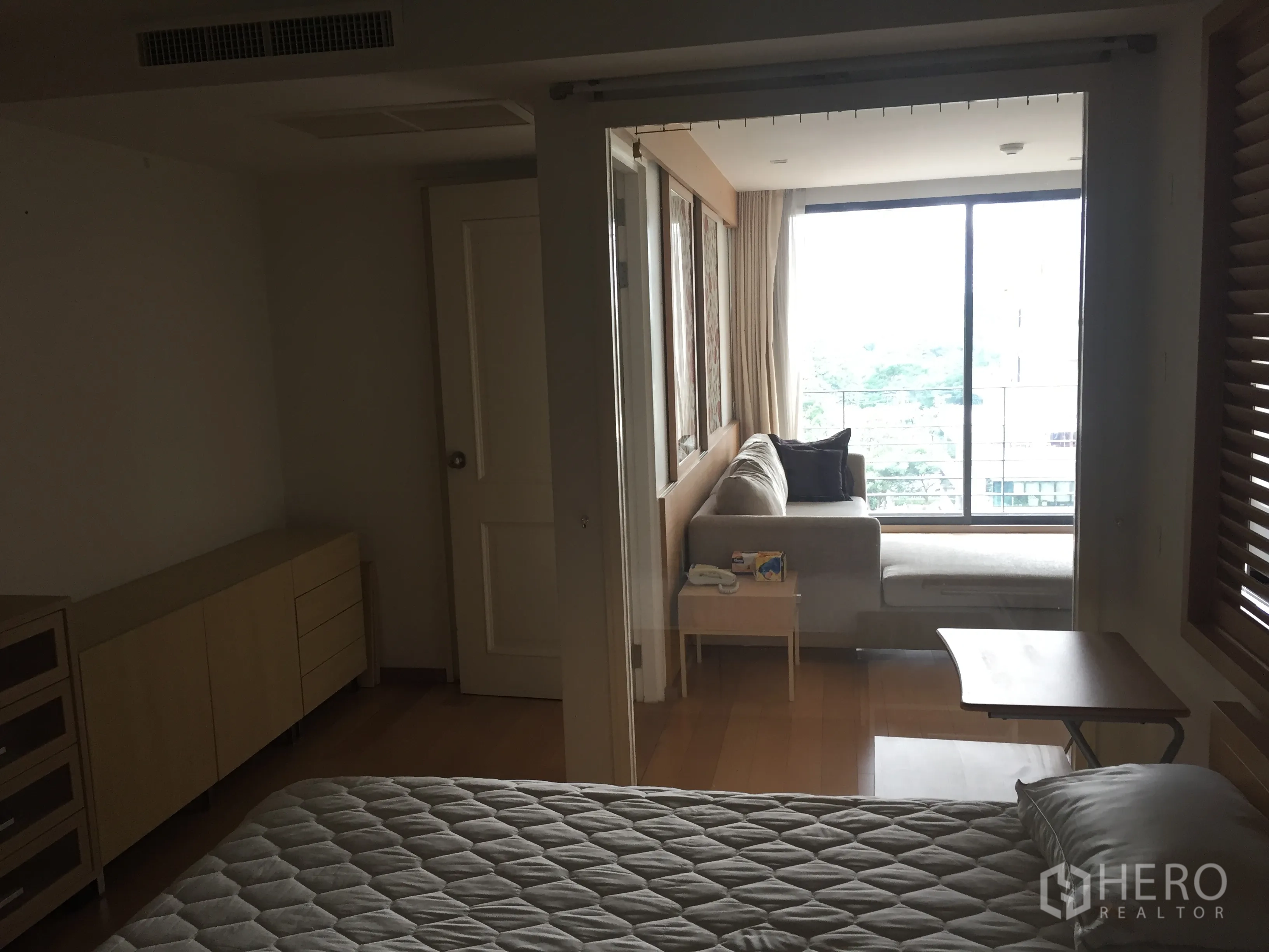 คอนโด ให้เช่าในPathum Wan, Bangkok - มุมมองจากห้องนอนไปยังห้องนั่งเล่นผ่านประตูกระจกบานเลื่อน มีโซฟามุมติดหน้าต่างเต็มบานพร้อมวิวพื้นที่สีเขียว