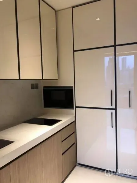 Condominium for rent in Khlong Toei, Bangkok - Compact kitchen with glossy cabinetry, built-in cooktop, microwave, and tall fridge.