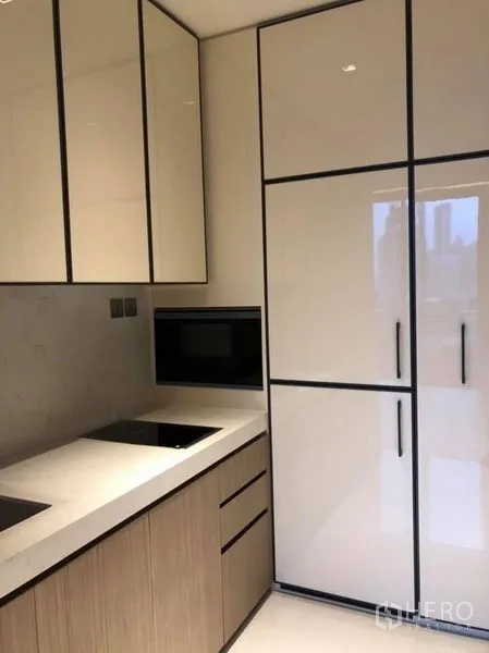 Condominium for rent in Khlong Toei, Bangkok - Compact kitchen with glossy cabinetry, built-in cooktop, microwave, and tall fridge.