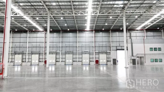 工厂 出租在Samut Prakan - 仓库墙面一排装卸门与调节板，旁有应急设备与人员门