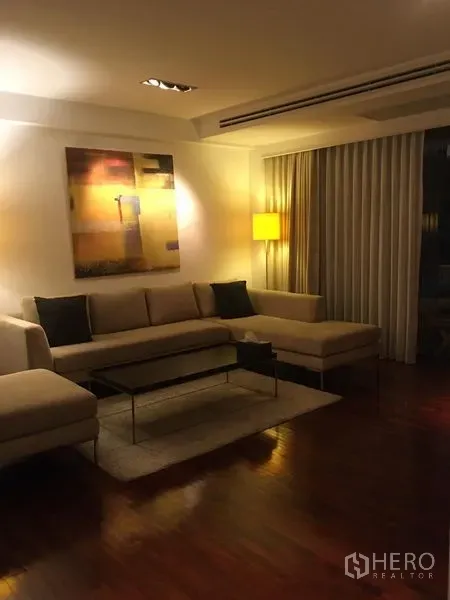 คอนโด ให้เช่า - ห้องนั่งเล่นสบายๆ โซฟาเข้ามุม โคมไฟตั้งพื้น งานศิลปะ และผ้าม่านสูงจรดเพดาน