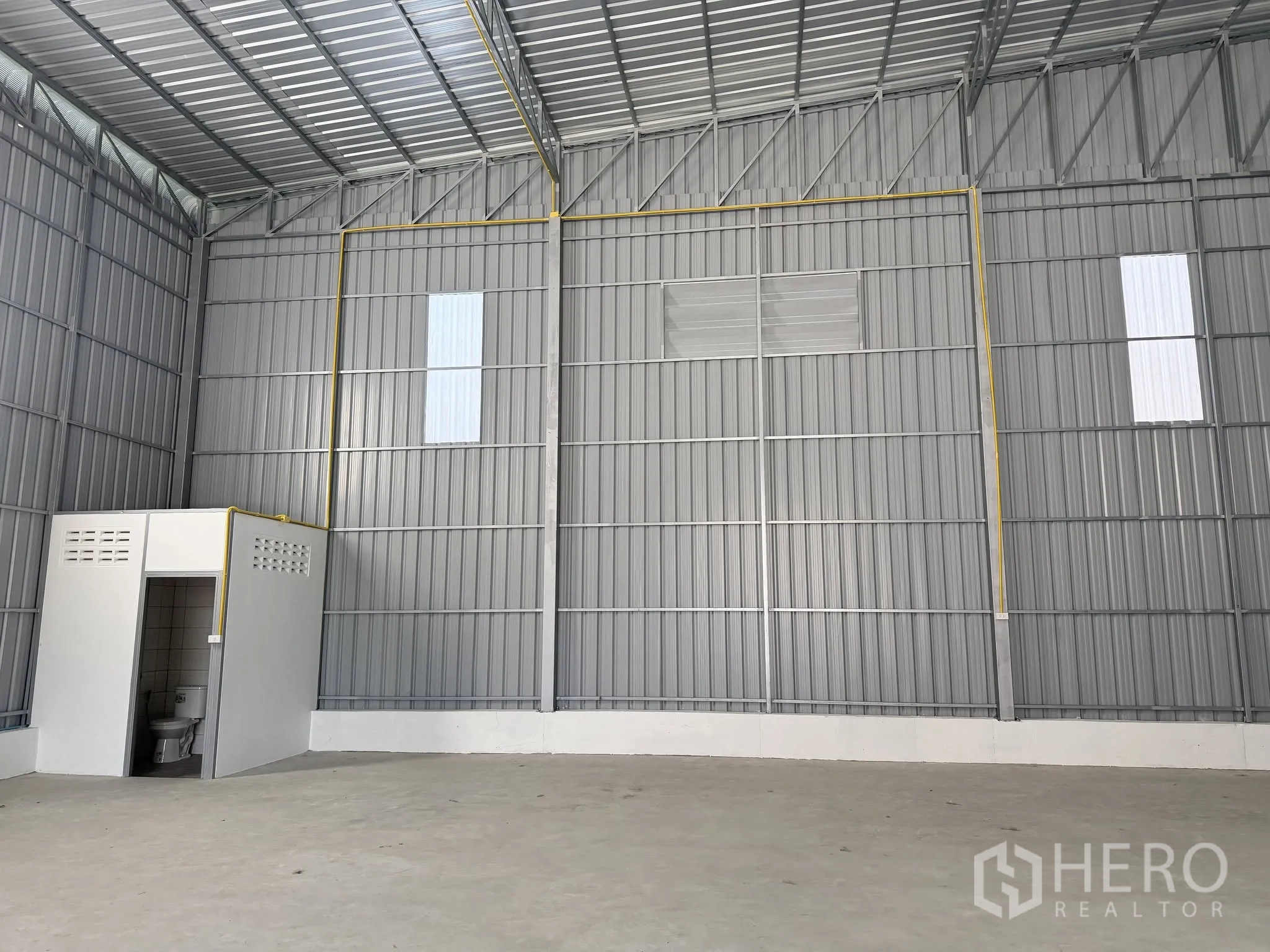 Warehouse for rent in Bang Kapi, Bangkok - Interior of metal-clad warehouse with high ceiling, concrete floor, and a built-in restroom.