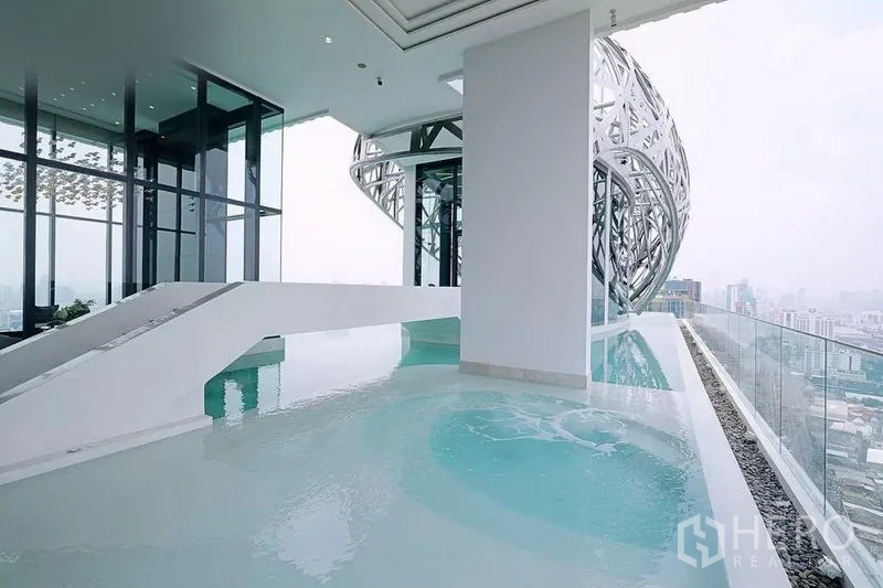 公寓 出租在Watthana, Bangkok - 屋顶无边际泳池，俯瞰天际线，旁有未来感金属外立面。