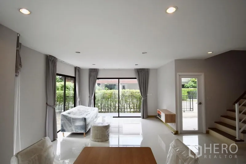 Detached House for rent in Prawet, Bangkok - Spacious living area with sliding glass doors to the patio and green hedge outside.