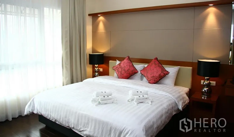Apartment for rent in Khlong Toei, Bangkok - Modern bedroom with king bed, accent pillows and warm wall sconces