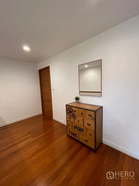 Townhouse for rent in Khlong Toei, Bangkok - Hallway corner with decorative chest, mirror and warm wood flooring.