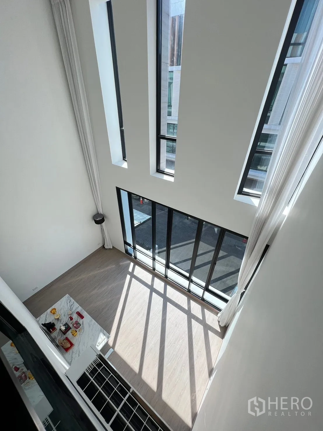 สำนักงานที่บ้าน ให้เช่าในChatuchak, Bangkok - มุมมองจากชั้นบนลงสู่ห้องนั่งเล่นเพดานสูง แสงธรรมชาติส่องผ่านช่องหน้าต่างยาวและประตูกระจกบานเลื่อน