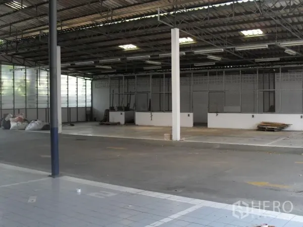 零售空间 出租在Khlong Toei, Bangkok - 带高金属屋顶的半仓储式区域，荧光灯照明，开阔的混凝土地面。