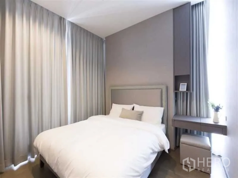 Condominium for rent in Bang Rak, Bangkok - Cozy bedroom with upholstered headboard, built-in desk and stool, and full-height curtains in soft neutral tones.